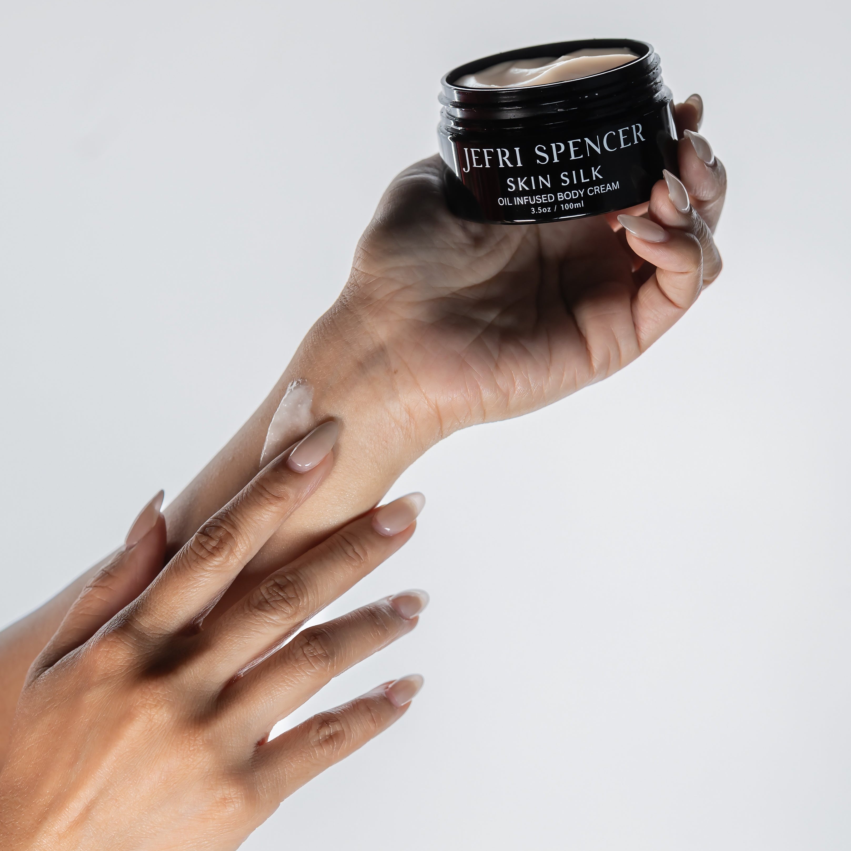 Hand applying cream from a Jefri Spencer jar on a light gray background