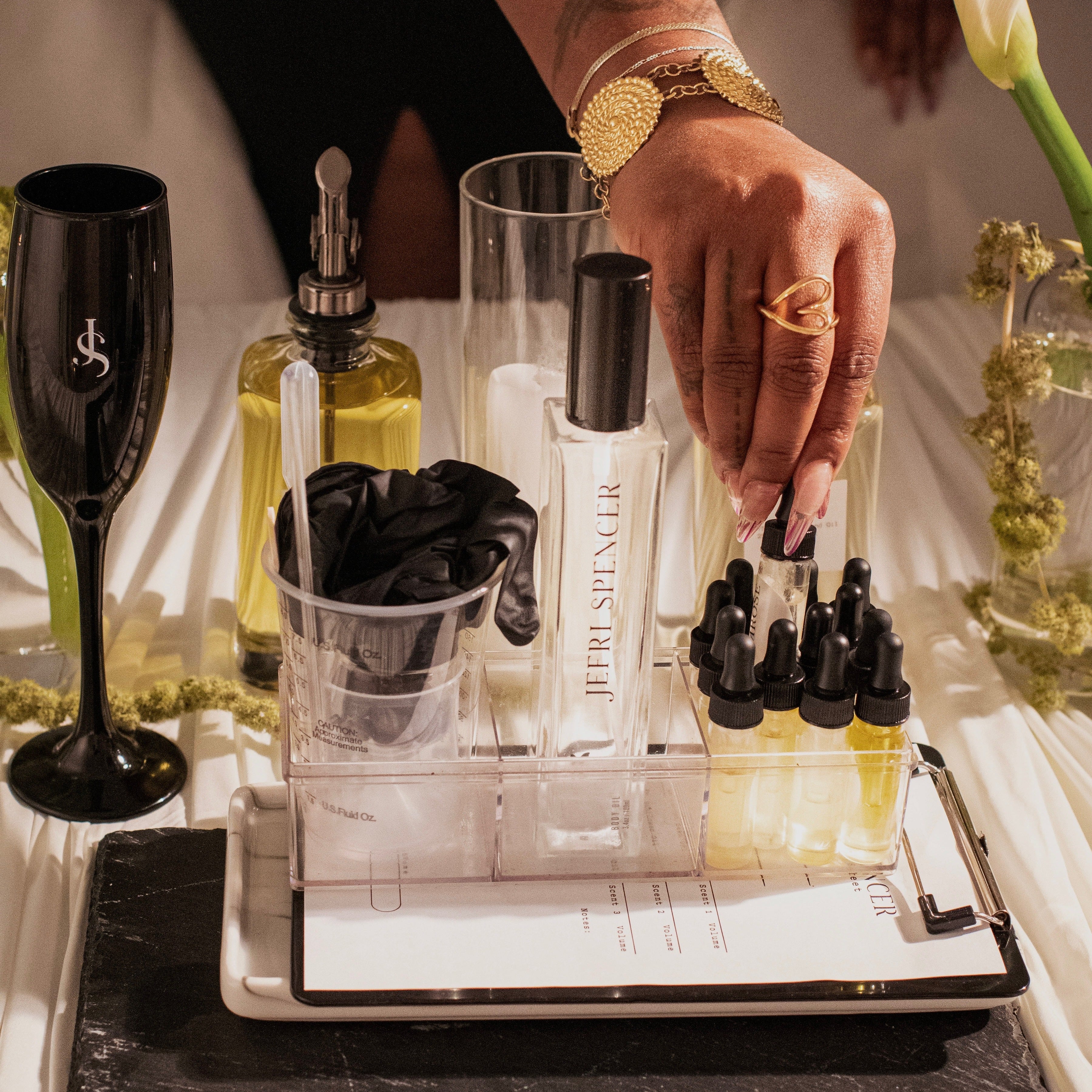 Hand selecting a perfume bottle from a display on a table with a black slate coaster.