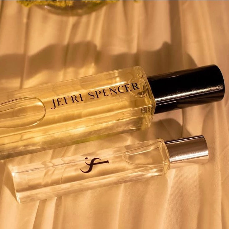 Two perfume bottles labeled 'Jefri Spencer' on a textured surface with a natural background.